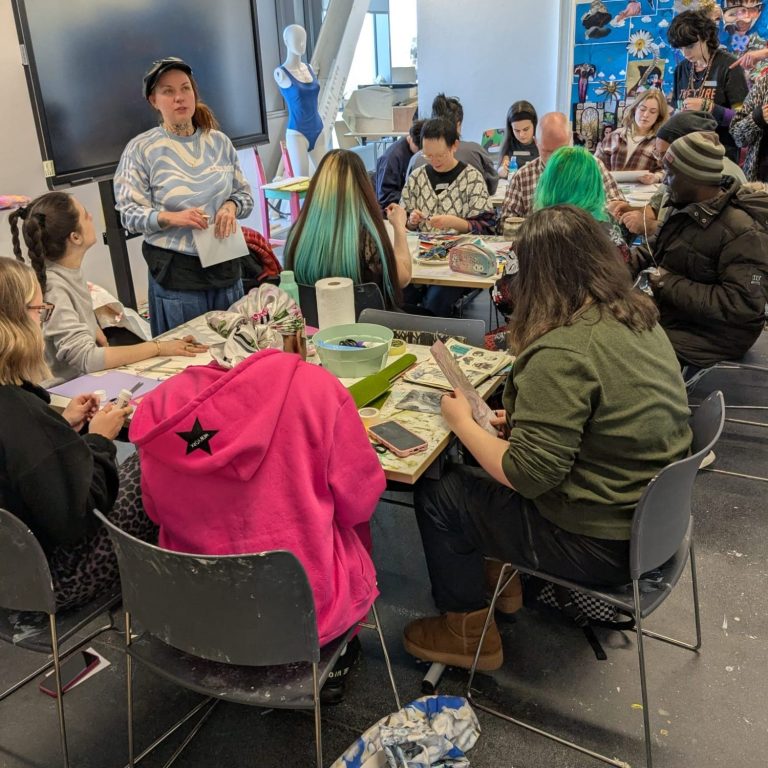 Art and Wellbeing Workshop Photo of two tables filled with art supplies, and surrounded by people making their own artwork