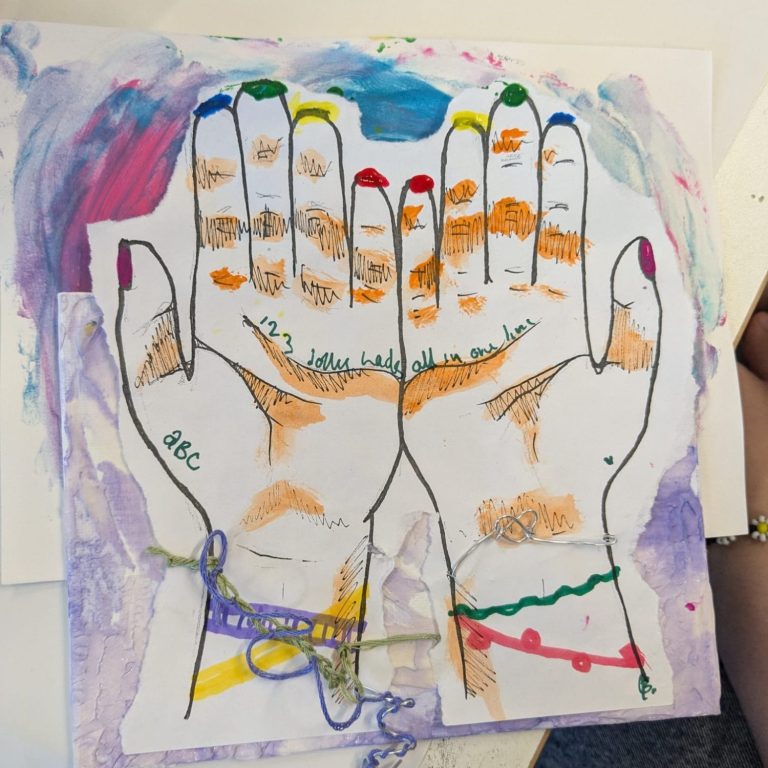 Community Art Group Photo of a pile of artwork, including a drawing of a rubix cube, colourful cut-out geometric shapes, and paperchain made of the same shapes