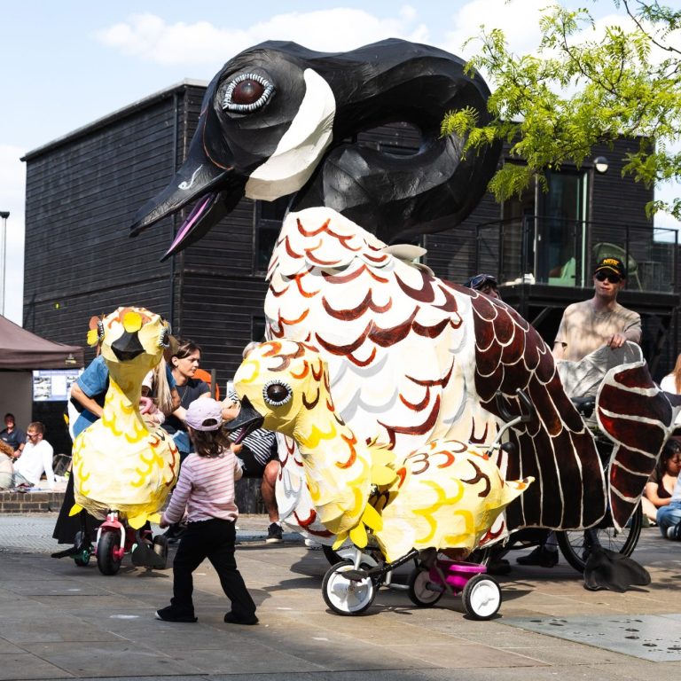 Middlewood Locks Fest Photo of a painted giant goose sculpture on wheels, twice the height of a man in the background, with two smaller yellow goslings in front