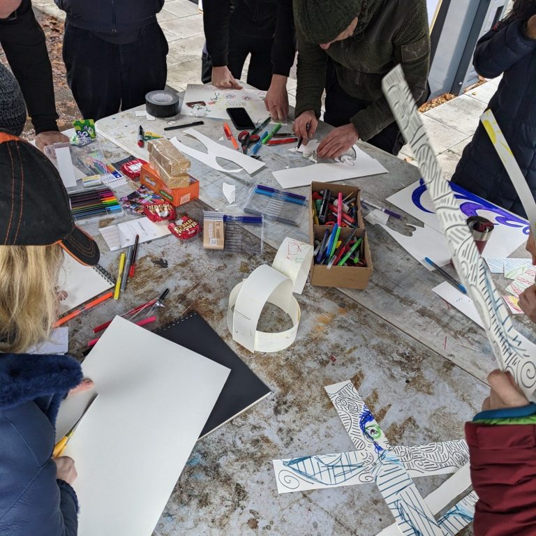 Community Art Group Photo of a pile of artwork, including a drawing of a rubix cube, colourful cut-out geometric shapes, and paperchain made of the same shapes