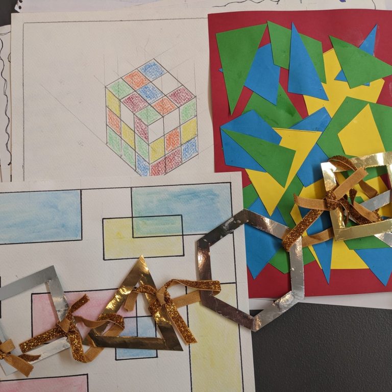 Community Art Group Photo of a pile of artwork, including a drawing of a rubix cube, colourful cut-out geometric shapes, and paperchain made of the same shapes